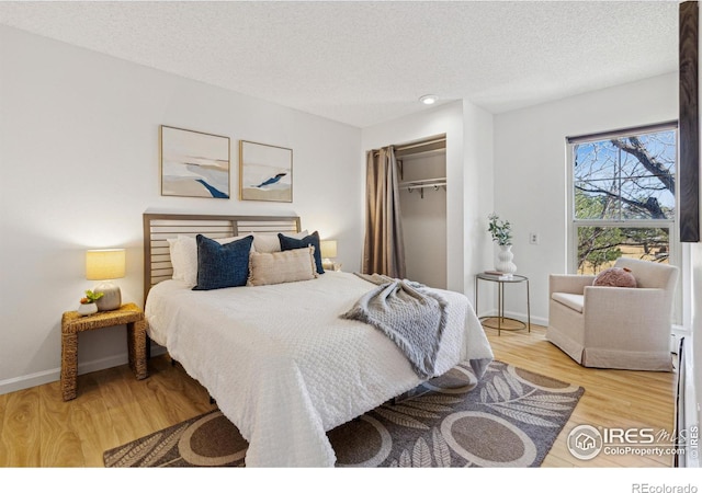 bedroom with a textured ceiling, light wood finished floors, a closet, and baseboards