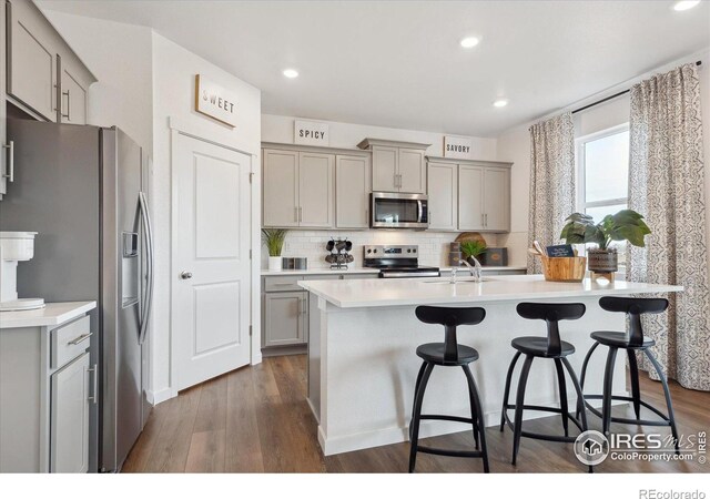 kitchen featuring stainless steel appliances, a breakfast bar, a sink, backsplash, and gray cabinets