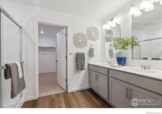 bathroom with double vanity, a sink, a shower stall, and wood finished floors