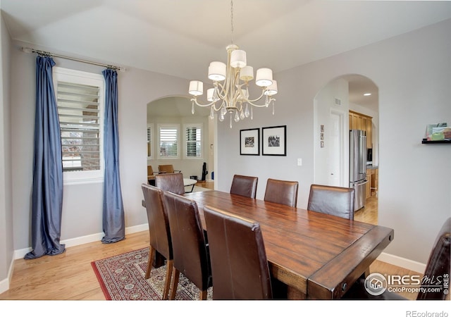 dining room featuring arched walkways, an inviting chandelier, light wood-style flooring, and baseboards