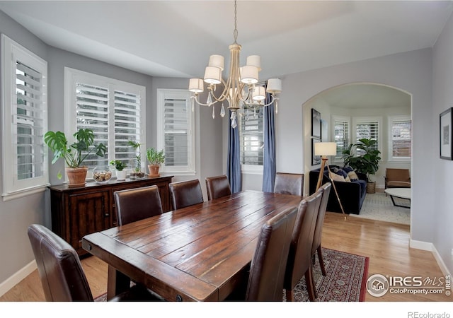 dining area featuring arched walkways, baseboards, a chandelier, and light wood-style floors