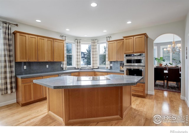 kitchen with arched walkways, black electric stovetop, stainless steel double oven, a center island, and light wood finished floors