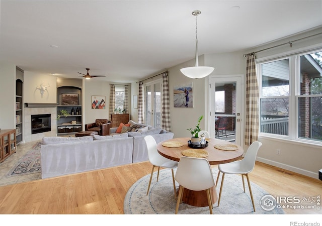 dining space featuring a wealth of natural light, baseboards, a tiled fireplace, and wood finished floors