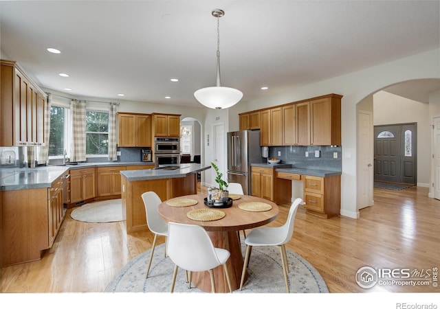 kitchen featuring light wood finished floors, arched walkways, decorative backsplash, a kitchen island, and appliances with stainless steel finishes