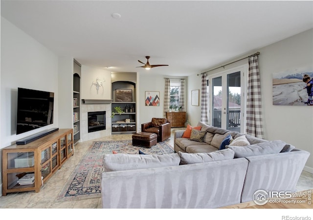 living room with ceiling fan, french doors, built in shelves, and a tiled fireplace