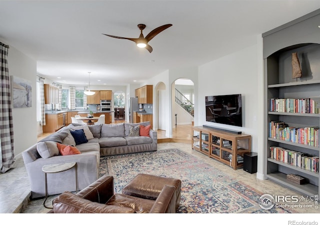 living room with built in features, arched walkways, ceiling fan, baseboards, and stairs