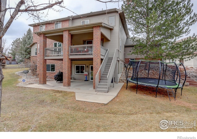 rear view of property featuring a patio, stairs, a trampoline, a yard, and brick siding