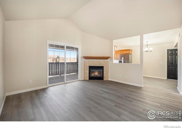 unfurnished living room featuring a tile fireplace, wood finished floors, baseboards, vaulted ceiling, and an inviting chandelier