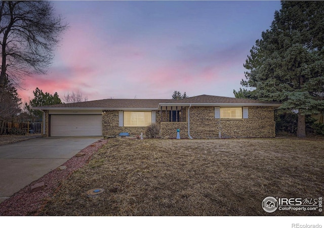 ranch-style home with a garage, concrete driveway, brick siding, and a front lawn