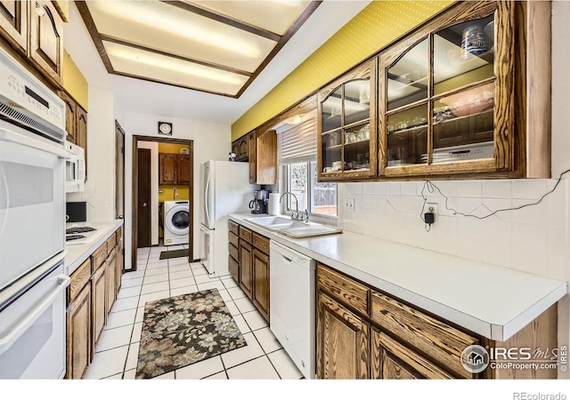 kitchen with white appliances, decorative backsplash, washer / clothes dryer, light countertops, and a sink