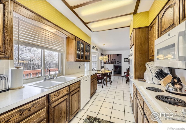 kitchen featuring light tile patterned floors, brown cabinetry, a sink, white appliances, and wallpapered walls