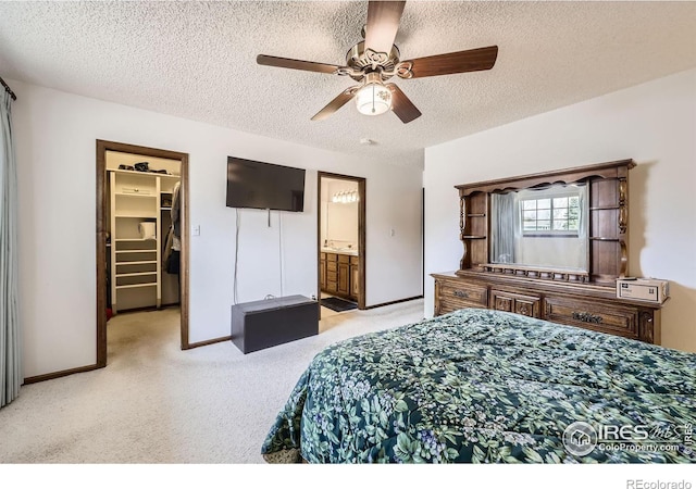 bedroom with light colored carpet, a spacious closet, ensuite bathroom, a ceiling fan, and a textured ceiling