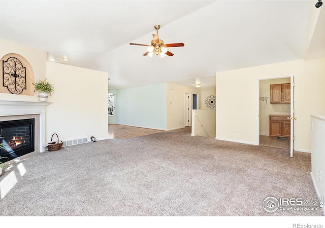 unfurnished living room with a tile fireplace, carpet floors, visible vents, a ceiling fan, and vaulted ceiling