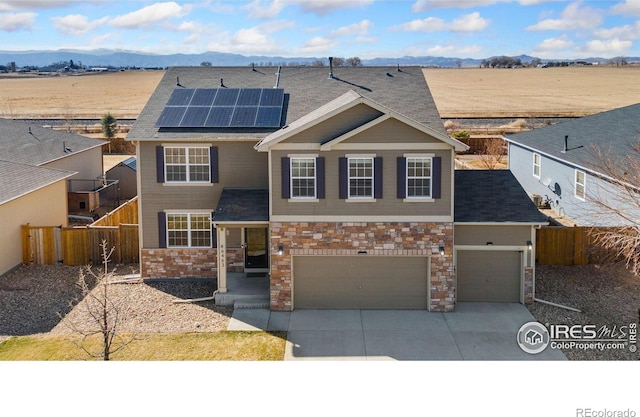 view of front facade with driveway, roof mounted solar panels, fence, a mountain view, and an attached garage