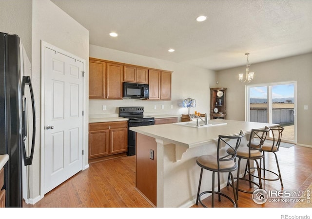 kitchen with a notable chandelier, black appliances, light wood-style flooring, a sink, and brown cabinetry