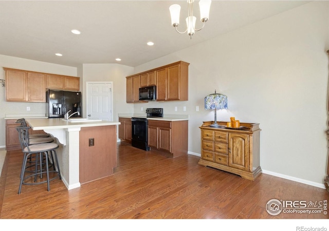 kitchen with light wood-type flooring, light countertops, a kitchen breakfast bar, a notable chandelier, and black appliances