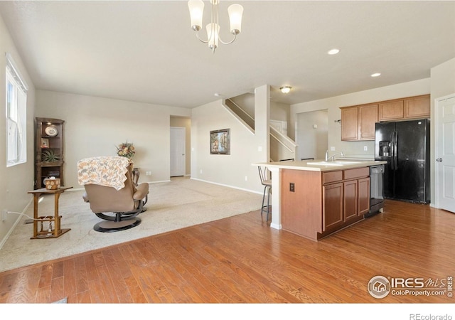 kitchen with dishwashing machine, an island with sink, light countertops, black fridge with ice dispenser, and open floor plan