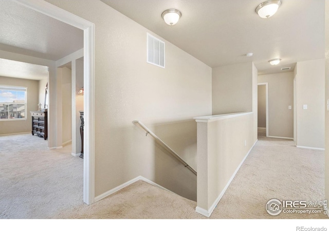 hall with an upstairs landing, carpet flooring, baseboards, and visible vents