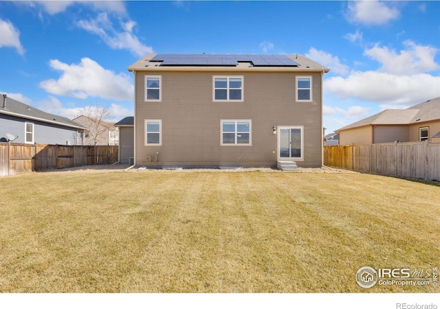 rear view of property with roof mounted solar panels, a lawn, and a fenced backyard