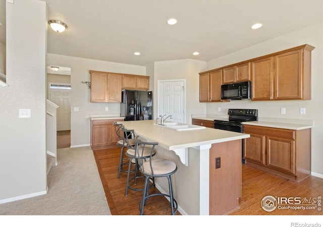 kitchen with a sink, light wood-style flooring, a kitchen breakfast bar, black appliances, and a kitchen island with sink