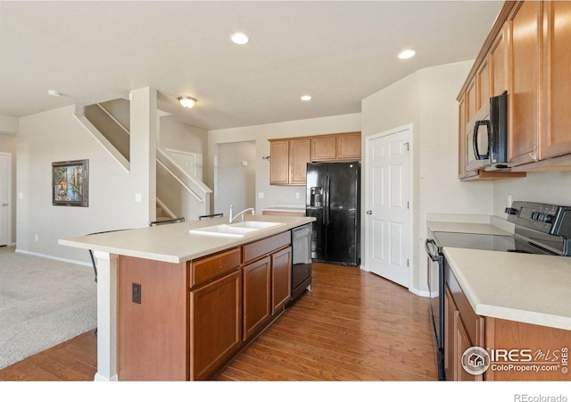 kitchen featuring black appliances, an island with sink, light countertops, and a sink