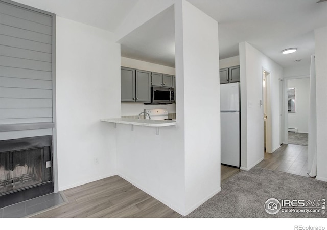 kitchen featuring range with electric cooktop, stainless steel microwave, freestanding refrigerator, light countertops, and light wood-type flooring