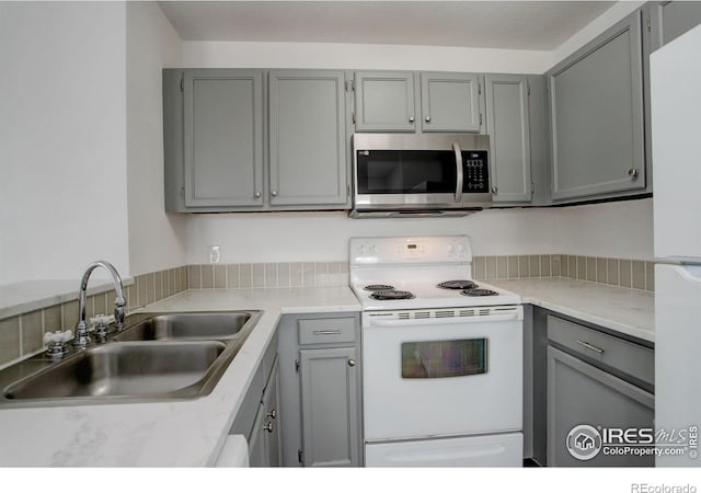 kitchen with white appliances, light countertops, a sink, and gray cabinetry