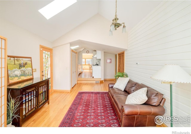 living room with a skylight, baseboards, a chandelier, wood finished floors, and high vaulted ceiling