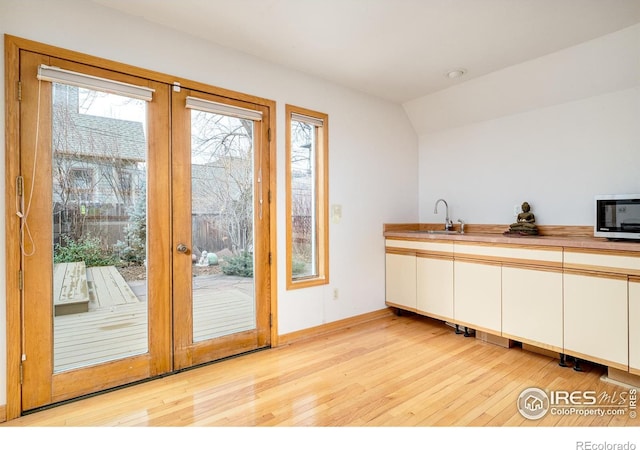 kitchen with light wood finished floors, french doors, stainless steel microwave, and a sink