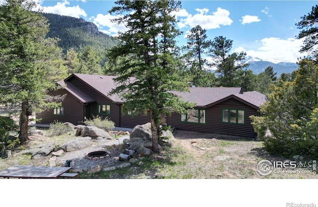 view of front of house featuring a forest view, an outdoor fire pit, faux log siding, and a mountain view