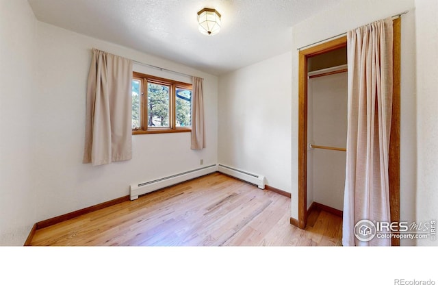 unfurnished bedroom featuring light wood finished floors, a baseboard radiator, and baseboards