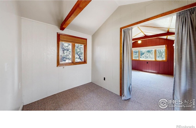 carpeted spare room featuring lofted ceiling with beams, a wealth of natural light, and wooden walls