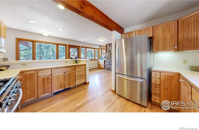 kitchen with appliances with stainless steel finishes, a wealth of natural light, beam ceiling, and light wood-style floors