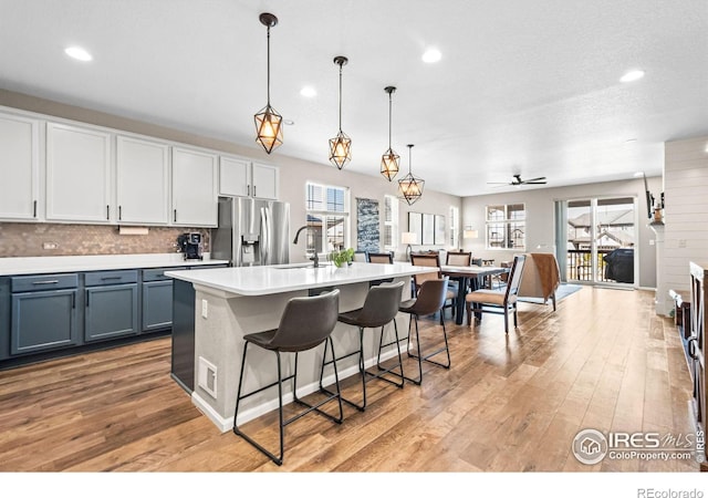 kitchen featuring stainless steel refrigerator with ice dispenser, light countertops, light wood-style floors, a sink, and a kitchen breakfast bar