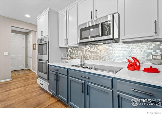 kitchen featuring light wood finished floors, stainless steel appliances, decorative backsplash, and light countertops