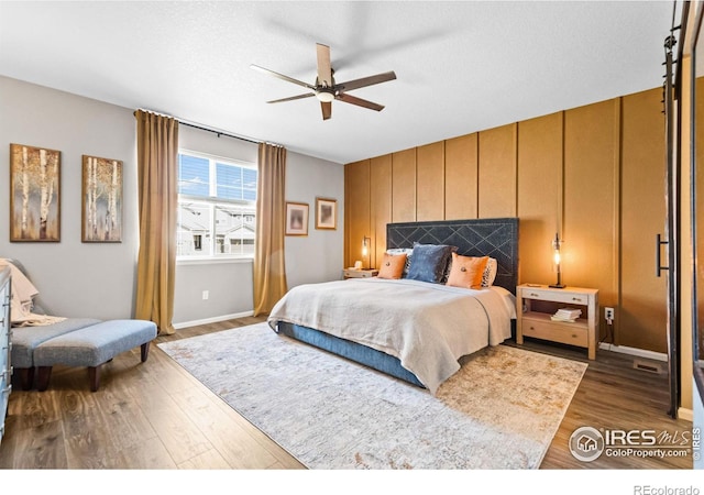 bedroom featuring ceiling fan, a textured ceiling, an accent wall, dark wood-type flooring, and baseboards