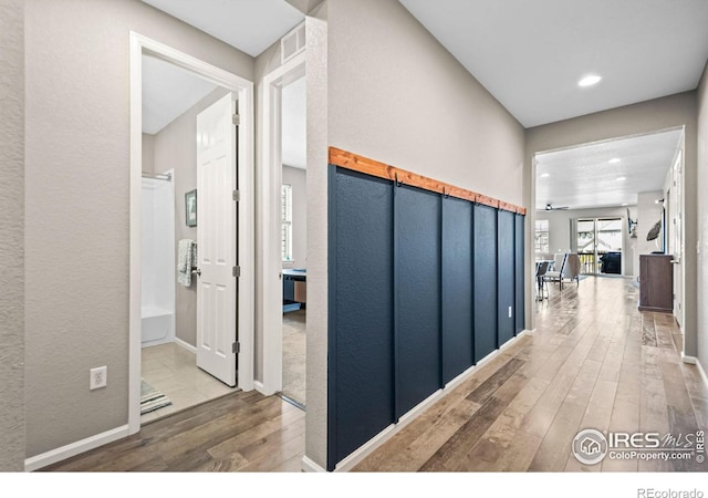 hallway featuring recessed lighting, visible vents, a textured wall, wood finished floors, and baseboards