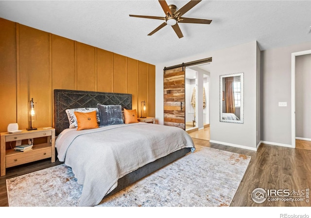 bedroom featuring a barn door, wood walls, wood finished floors, a ceiling fan, and baseboards