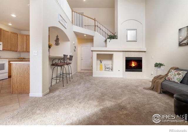 living room featuring light carpet, a tiled fireplace, a towering ceiling, light tile patterned flooring, and recessed lighting