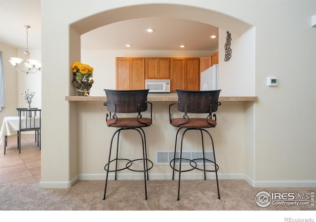 kitchen featuring arched walkways, a breakfast bar area, recessed lighting, light carpet, and white appliances