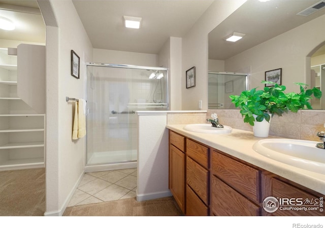 bathroom with double vanity, a shower stall, visible vents, and a sink