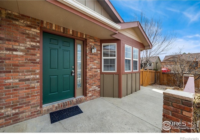 view of exterior entry featuring brick siding, fence, and board and batten siding