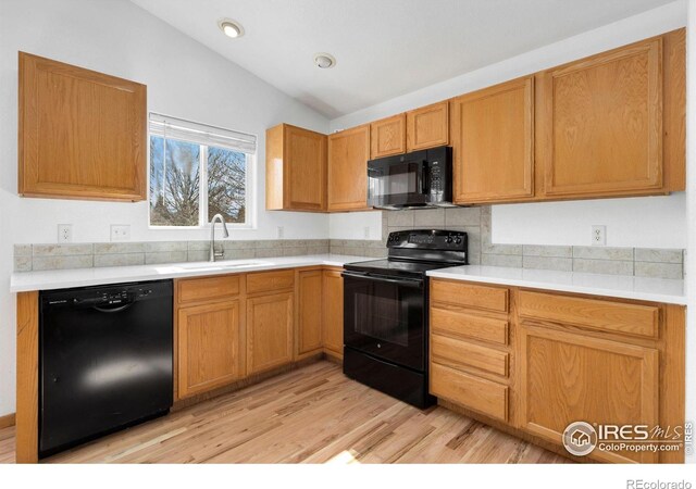 kitchen with a sink, black appliances, light countertops, and vaulted ceiling