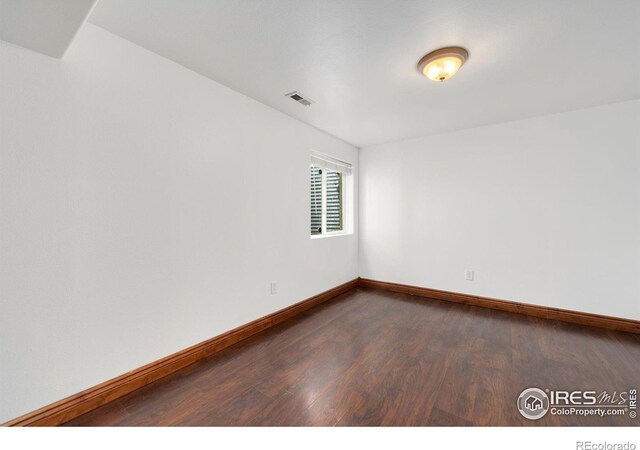 spare room featuring dark wood-style floors, visible vents, and baseboards