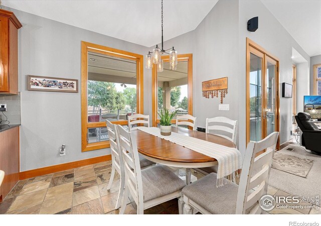 dining space featuring lofted ceiling, french doors, stone finish floor, and baseboards