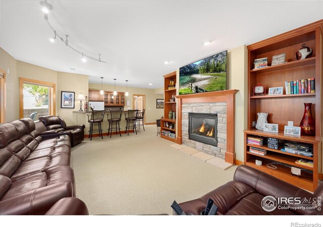 carpeted living room featuring baseboards, a stone fireplace, bar area, and track lighting