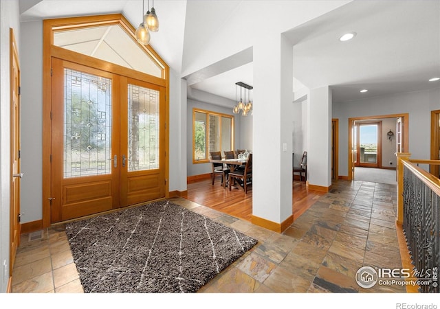 entrance foyer with baseboards, lofted ceiling, an inviting chandelier, stone tile flooring, and french doors