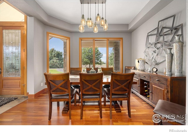 dining area with a raised ceiling, a notable chandelier, light wood-style flooring, and baseboards