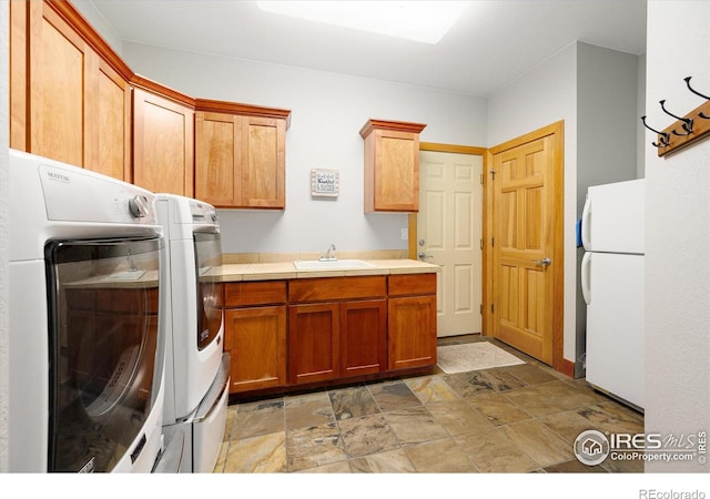 clothes washing area featuring washing machine and dryer, stone finish flooring, cabinet space, and a sink