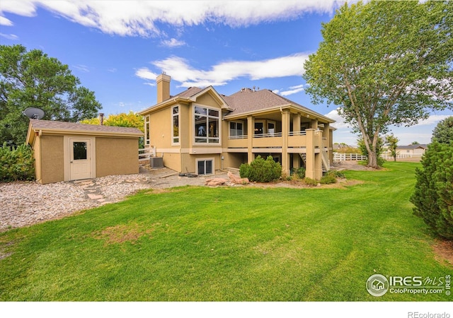 back of house featuring a chimney, a yard, central air condition unit, an outdoor structure, and stucco siding